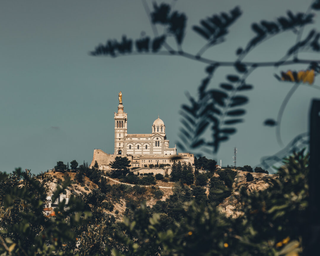 404 1 Vue artistique de la basilique Notre-Dame de la Garde à Marseille, capturée à travers des feuillages en premier plan.