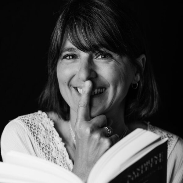 Photographe Portrait Marseille 4 Portrait noir et blanc d’une femme souriante tenant un livre, capturant un moment de spontanéité et de complicité à Marseille.